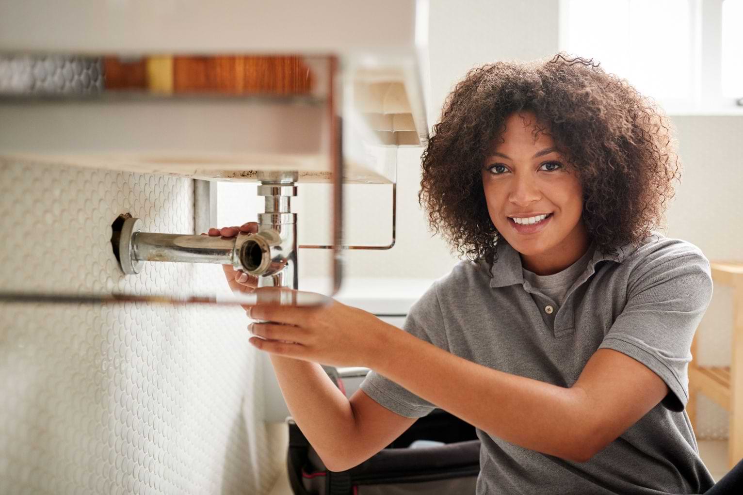 Young black female plumber sitting on the floor fixing a bathroom sink